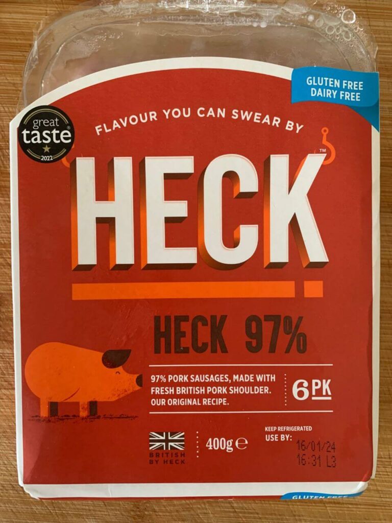 Packaging for HECK 97% pork sausages, featuring a bold orange and red label. The product has a 'Great Taste 2022' badge, and highlights that it is gluten and dairy free. There's an illustration of a pig, and text stating the sausages are made with fresh British pork shoulder following their original recipe. The pack size is 400g and it's marked to keep refrigerated with a use by date.