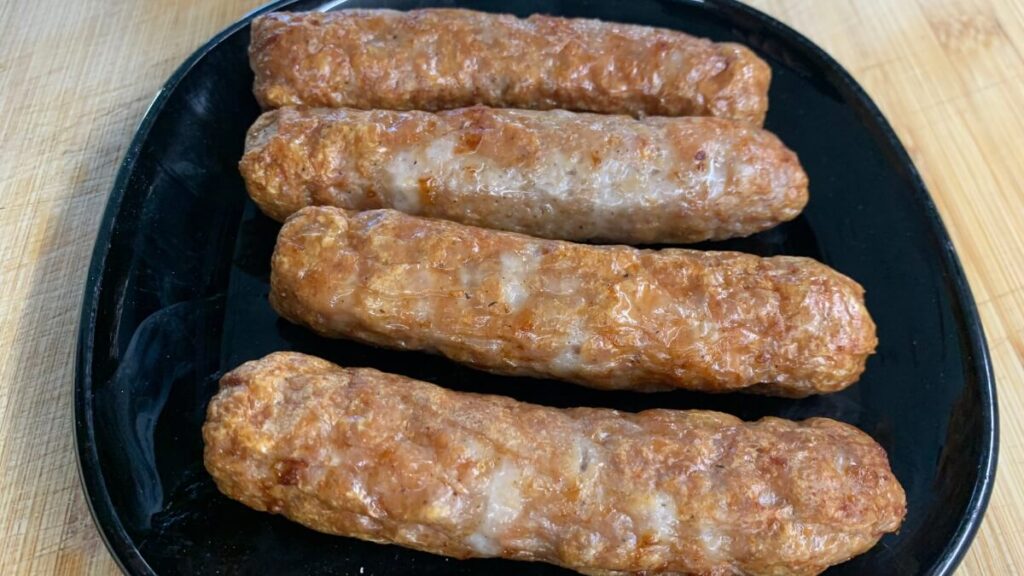 Another close-up of the cooked sausages on a black plate, taken from a slightly different angle, showing the browned and crispy exterior of the sausages in more detail and from a higher perspective.