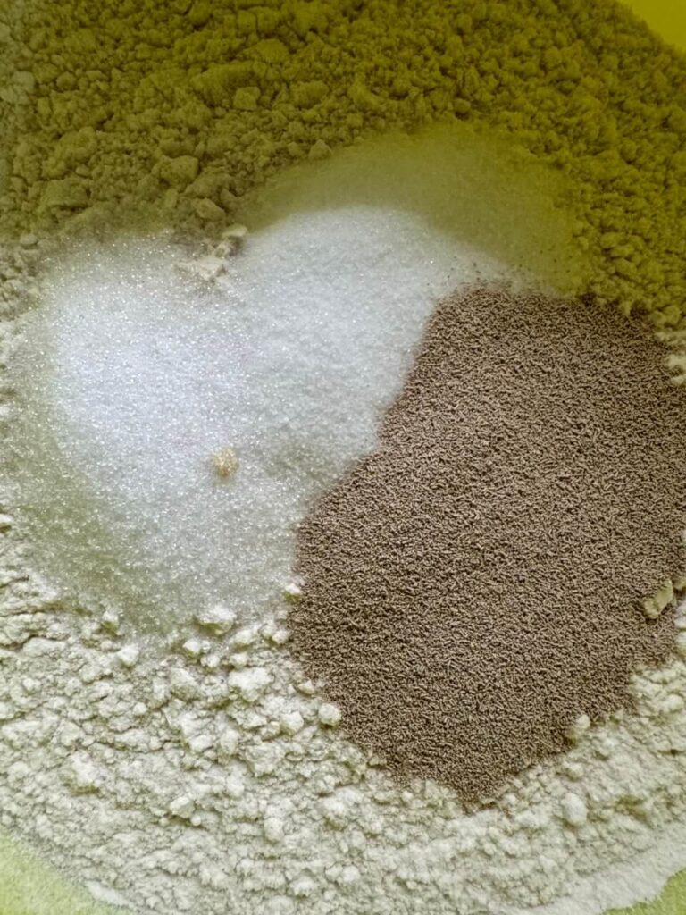 The initial step of bread-making with ingredients combined in a bowl. The dry flour mix is visibly separated from the salt and sugar on one side and yeast on the other, creating a stark contrast of textures and colors