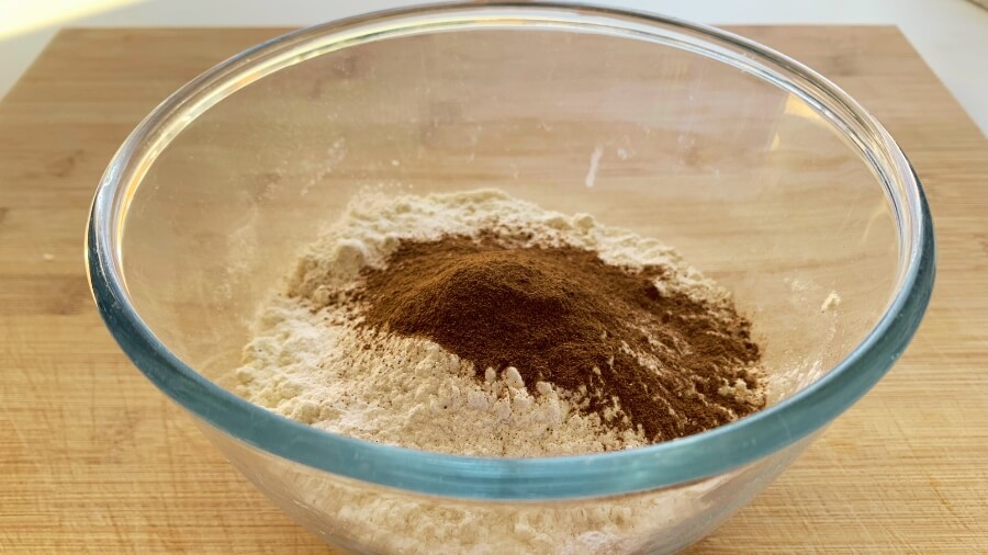 A close-up of dry ingredients in a glass bowl, with flour and a mound of cinnamon ready to be mixed for donut hole dough.