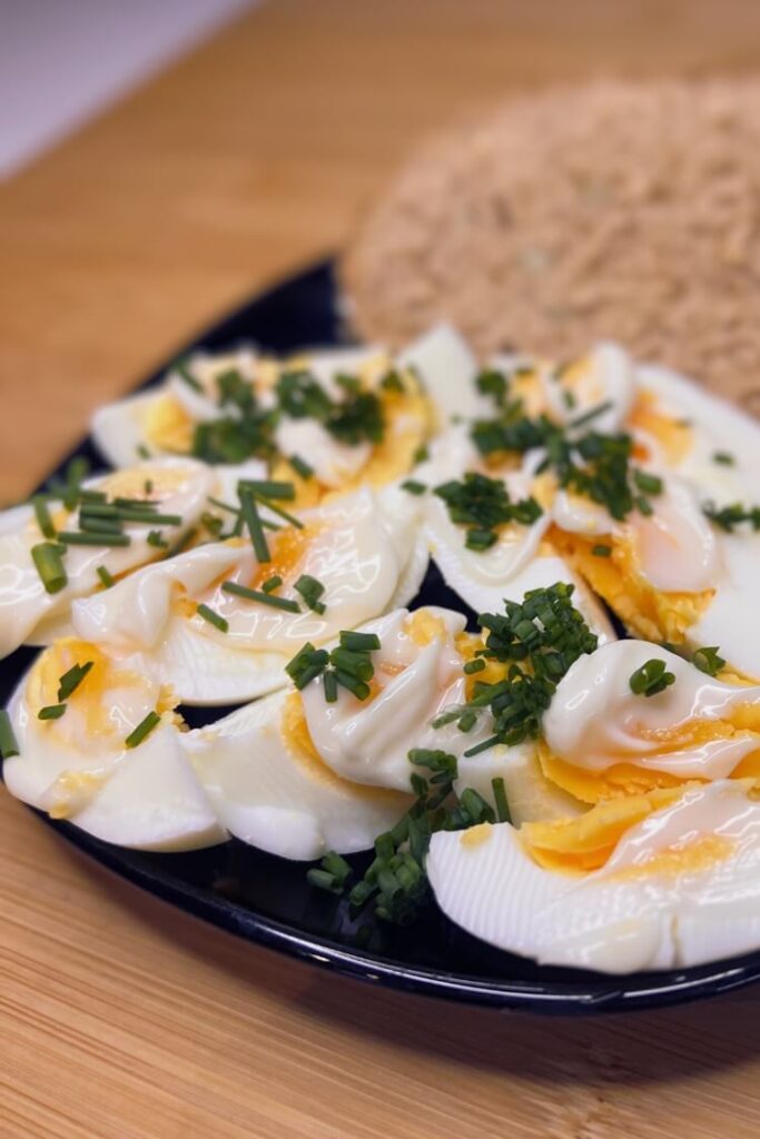A plate of air fryer hard-boiled eggs cut in halves, topped with mayonnaise and a sprinkle of fresh chives, on a wooden tabletop.