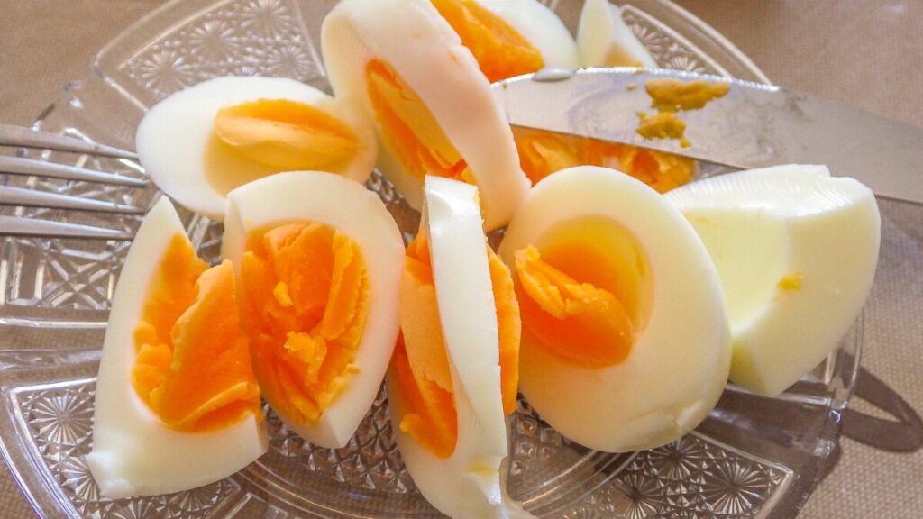 The image displays a plate with sliced hard-boiled eggs, their bright orange yolks visible. A knife rests on the plate, which features a decorative pattern. The setting suggests the eggs are ready to be served.