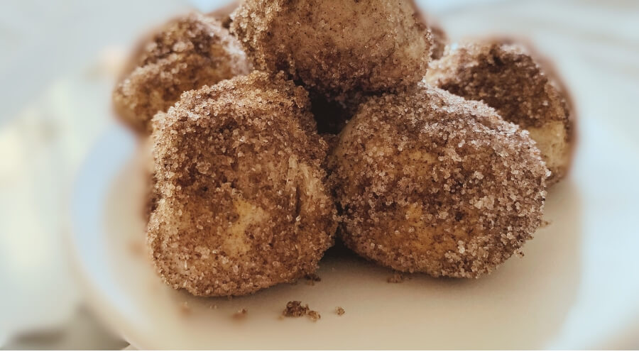 A plate of cinnamon sugar-coated homemade donut holes, ready to be enjoyed, presented on a wooden surface.