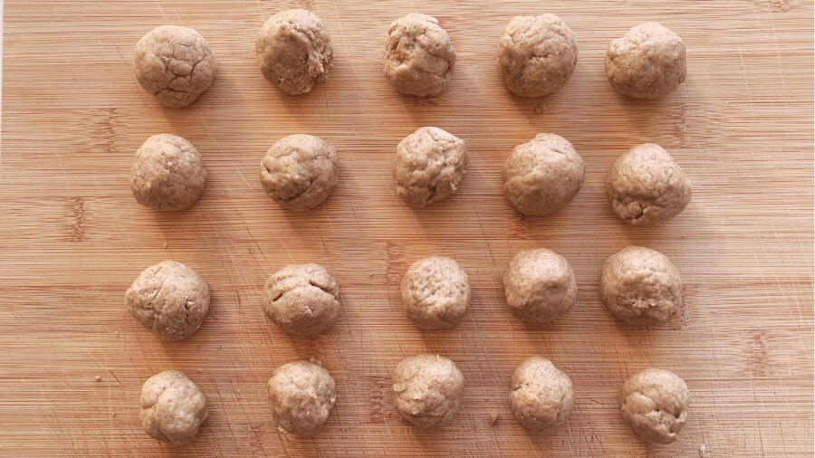 Rows of small, round, unbaked homemade donut hole dough pieces laid out on a wooden surface, prepared for cooking.